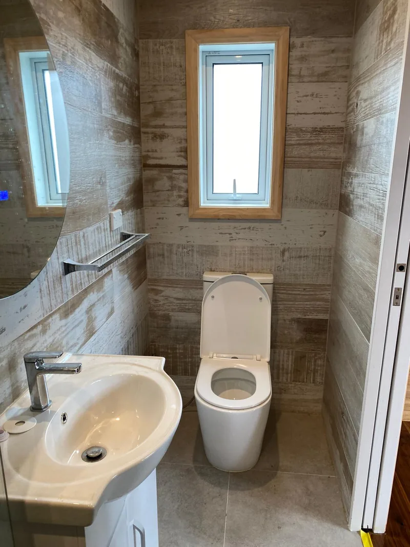 Bathroom with timber-look tiles, white basin and toilet beside a tall window