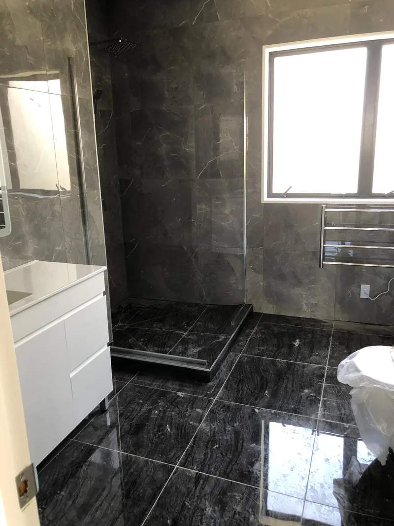 Dark stone-look tiled bathroom with a white vanity, window and shower area during renovation