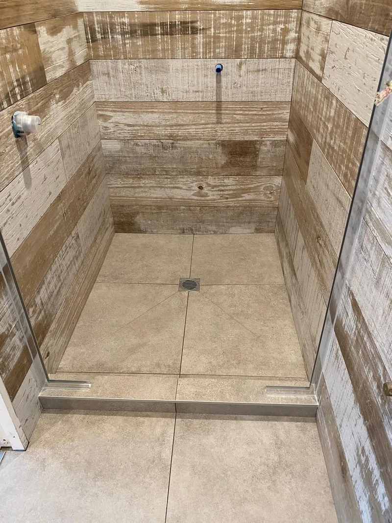 Tiled shower floor and drain surrounded by timber-look wall tiles and a glass enclosure
